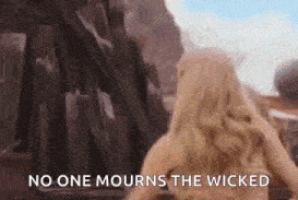 a woman is standing in front of a building with the words `` no one mourns the wicked '' written on the screen .
