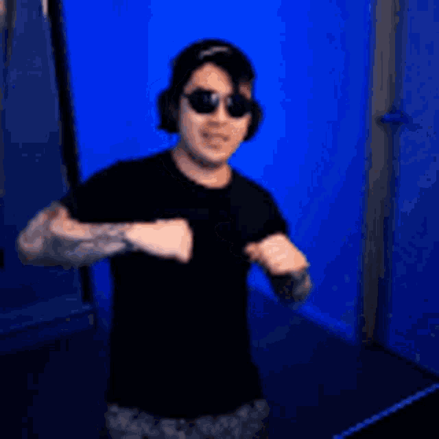 a man wearing a black shirt and sunglasses is standing in front of a blue wall .