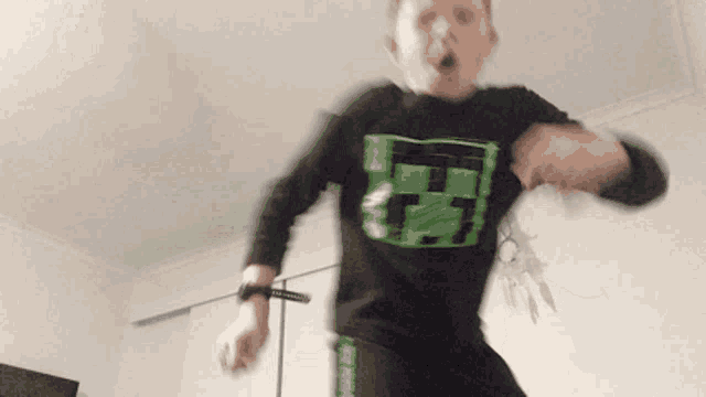 a young boy wearing a black shirt with a green minecraft logo on it is dancing in a room .