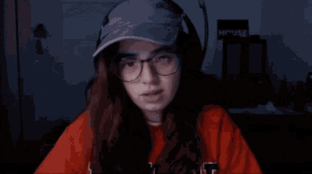 a girl wearing glasses and a hat is laughing in front of a sign that says house