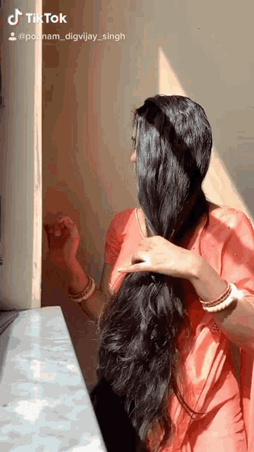 a woman with very long black hair is standing in front of a wall with a tiktok logo on the bottom