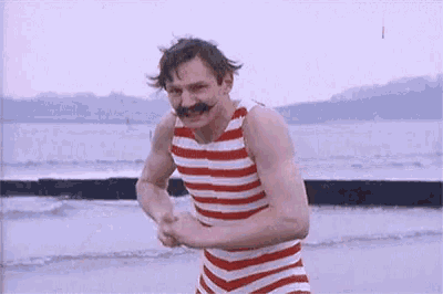 a man in a red and white striped bathing suit with a mustache is standing on a beach .