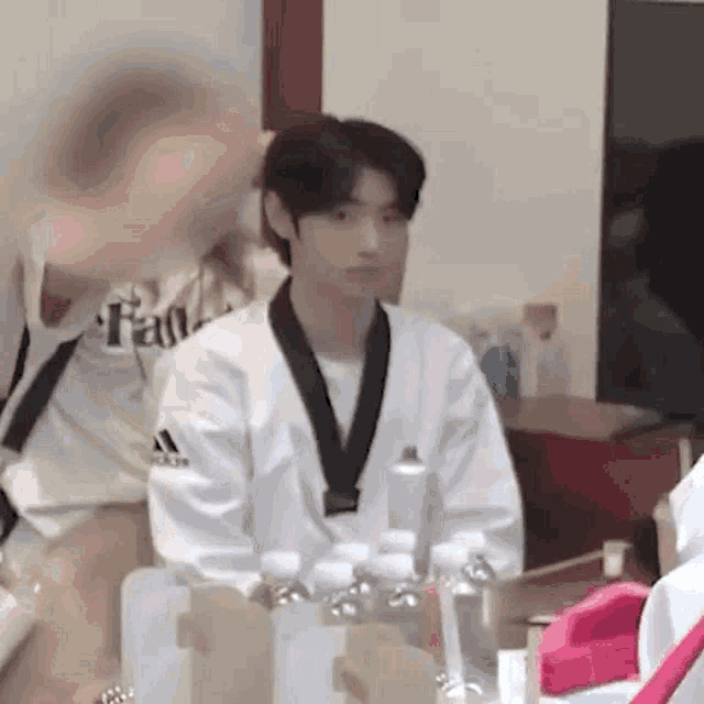 a young man in a taekwondo uniform is sitting in a room with bottles of water .