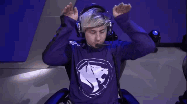 a man wearing headphones and a purple sweatshirt is sitting in a chair with his arms outstretched .