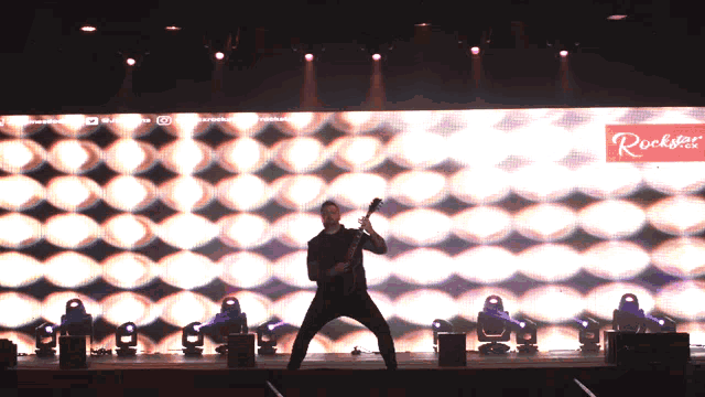 a man playing a guitar on a stage in front of a rockstar sign