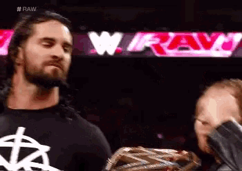 a man with a beard is standing next to another man holding a wrestling championship belt .