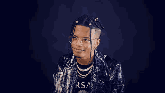 a man wearing glasses and a versace shirt smiles