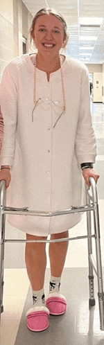 a woman in a white coat and pink slippers is standing next to a walker .