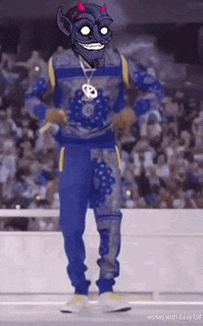 a man in a blue outfit with a devil mask on his face is dancing in front of a crowd .