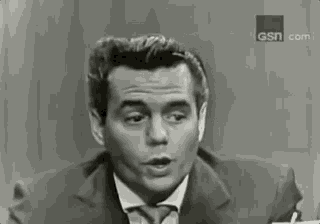 a man in a suit and tie is talking in front of a sign that says gsn.com