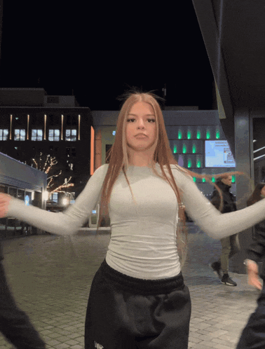 a woman in a white top is dancing in front of a building