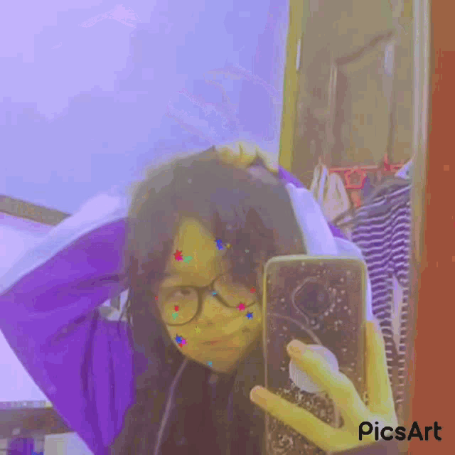 a girl is taking a picture of herself in a mirror while wearing glasses and a purple hoodie .
