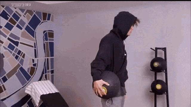 a man in a black hoodie is holding a black ball in a gym