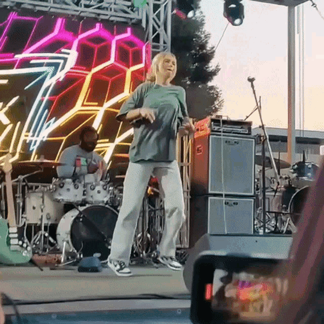 a woman is dancing on a stage with a man playing drums in the background