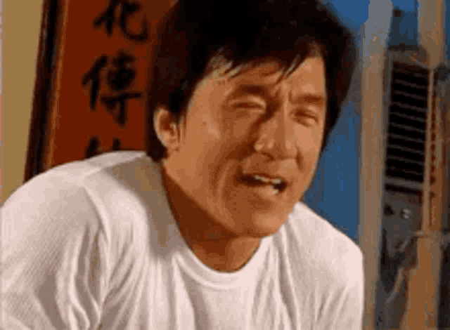 a man in a white shirt is crying with his eyes closed and a sign in the background .