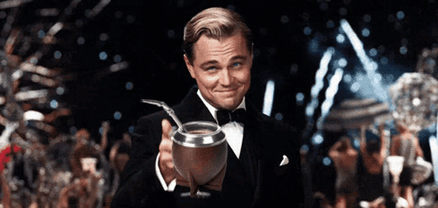a man in a tuxedo is holding a silver cup with a straw in it