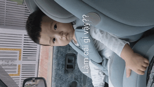 a baby sitting in a car seat with the words " lam cai gi vay " written on the bottom