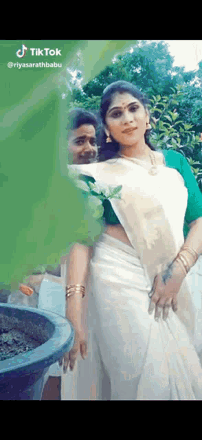 a woman in a white saree with a green blouse is standing next to a man in a green shirt .