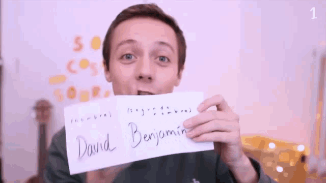 a man is holding a piece of paper with the name david benjamin written on it