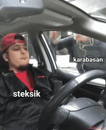 a man in a red hat is driving a car with the words karabasan steksik on the steering wheel