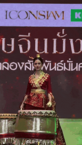 a woman in a red and gold costume stands in front of a sign that says iconsiam