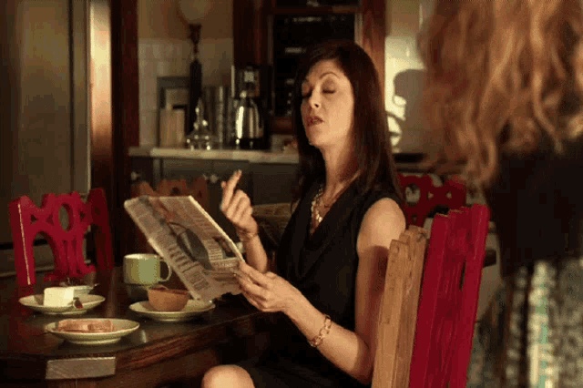 a woman sits at a table reading a newspaper with a picture of a man on it