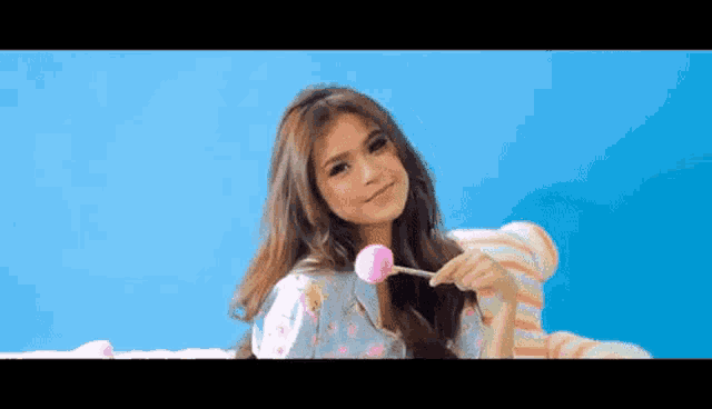 a young woman is holding a pink lollipop in her hand .