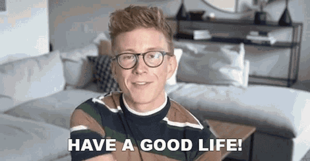 a man with glasses is sitting on a couch in a living room .