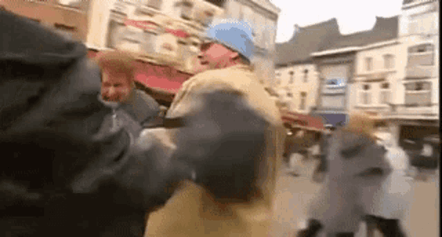 a man in a blue hat is dancing in a crowd of people on a city street .