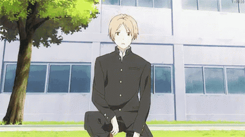 a man in a school uniform is sitting on the grass in front of a building .