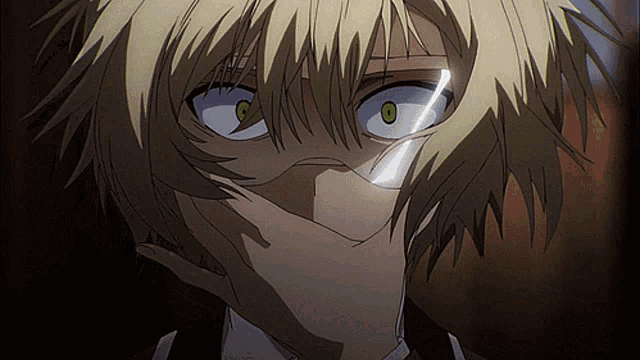 a man with blonde hair and green eyes covering his face with his hand