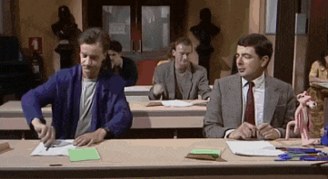 a group of men are sitting at desks in a classroom with a pink panther in the background .