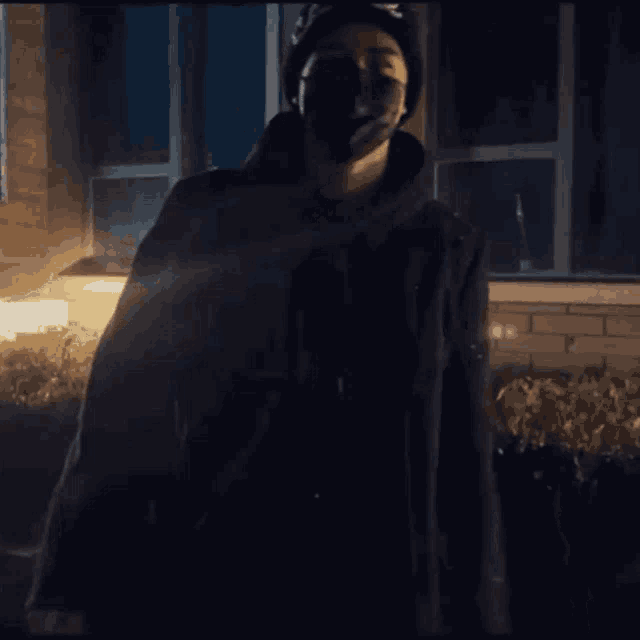 a man wearing a black mask and a black jacket stands in front of a building
