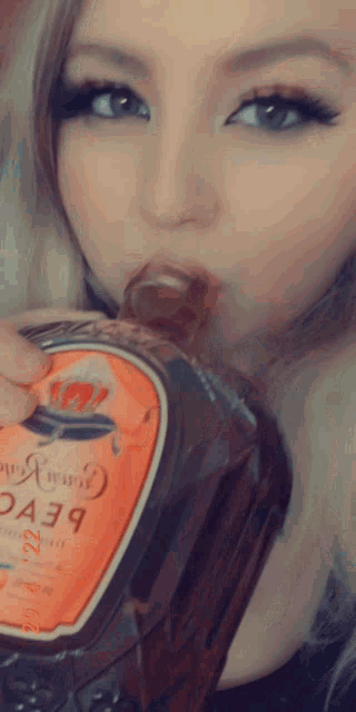 a woman drinking from a bottle that says crown royal on it