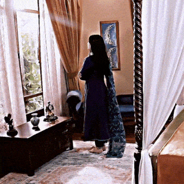 a woman in a purple dress stands in front of a canopy bed