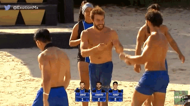 a group of men are standing on a sandy beach with a screen that says exation mx