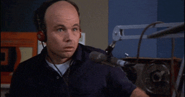 a bald man wearing headphones is pointing at something in front of a microphone .