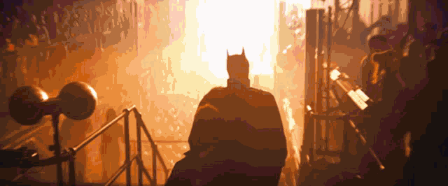 a silhouette of a man in a bat suit stands in front of a fire