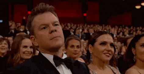 a man and a woman are smiling while sitting in a crowd of people at an awards show .