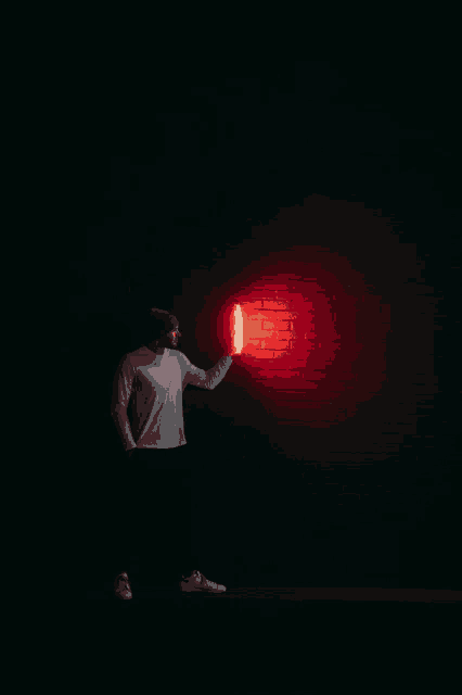 a man in a suit holds a red light in front of a brick wall