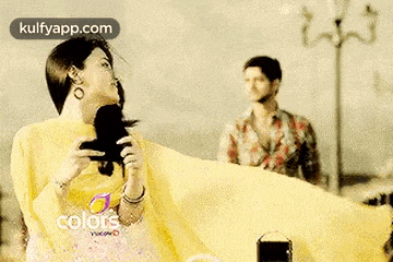 a woman in a yellow dress is taking a picture of a man standing behind her .