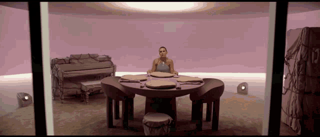 a woman sits at a table in a room with a pink wall