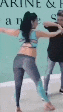 a woman in a blue top and gray leggings is dancing with a man in a black shirt .