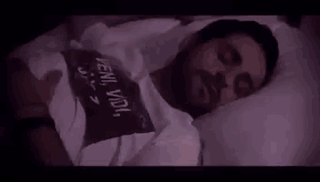 a man with a beard is sleeping in a bed with a t-shirt on .