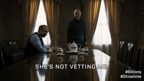 two men are sitting at a long table with a caption that says " she 's not vetting me "
