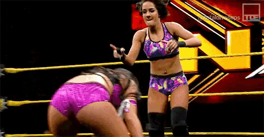 two women are wrestling in a wrestling ring and one of them is pointing at the other .