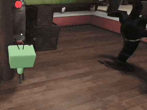 a green cube is sitting on a wooden floor next to a black object