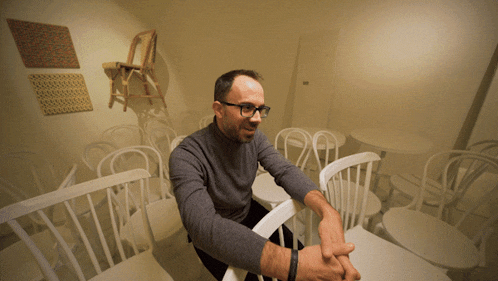 a man wearing glasses sits on a white chair