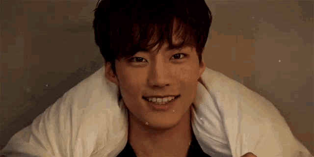 a young man with a white towel wrapped around his neck is smiling .