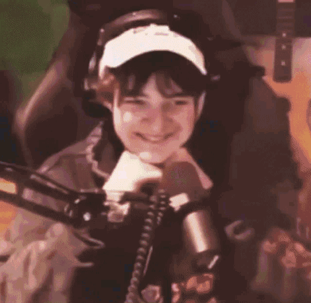a person wearing headphones and a hat is sitting in a chair in front of a microphone .